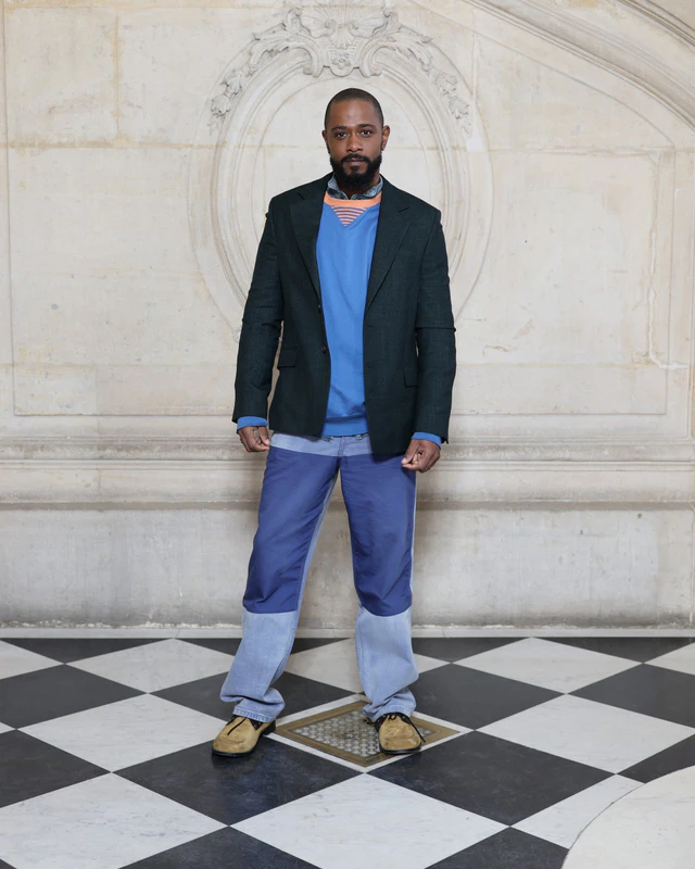 ディオール 2026-2027年ウィンター コレクション ラキース・スタンフィールドはダークグレーウールのノッチドラペルジャケットと、ブルーのジャージープルオーバー、ブルーのコットンパンツを着用しました。ディオールのアクセサリーも身につけました。