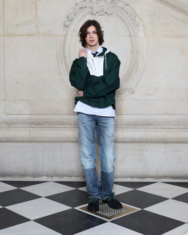 ディオール 2026-2027年ウィンター コレクション ポール・キルヒャーはディオールのグリーンレインコートと、ブルーストライプコットンシャツ、ブルーデニムジーンズを着用しました。ディオールのアクセサリーも身につけました。