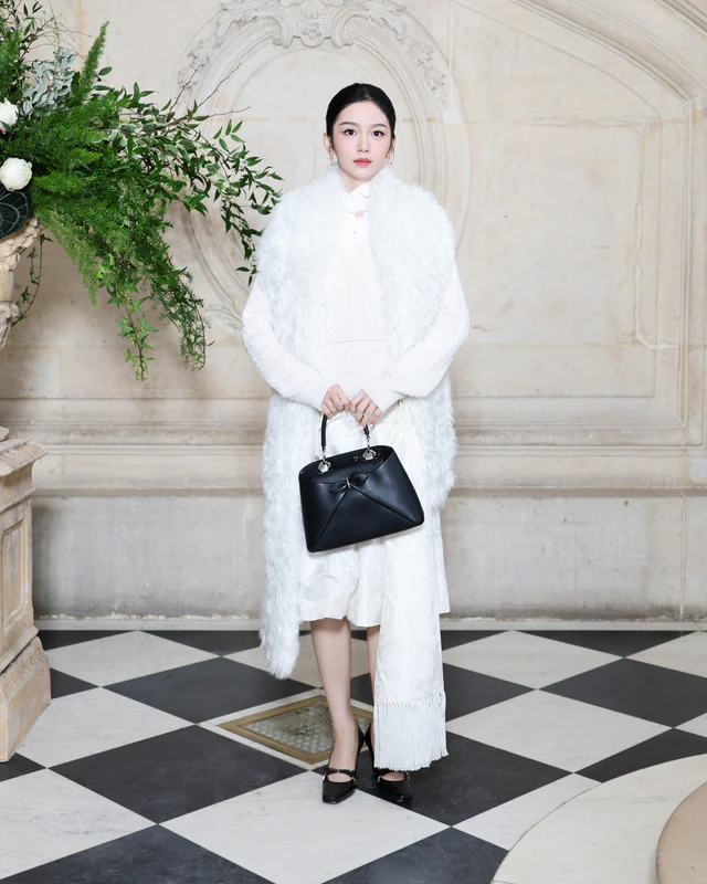 ディオールの2026年春夏オートクチュール コレクションでジョウ・イエは、2026年フォール コレクションより、ホワイトのフェイクファースカーフを、ホワイトのウールカーディガン、コットンシャツ、シルクスカートと合わせて纏いました。